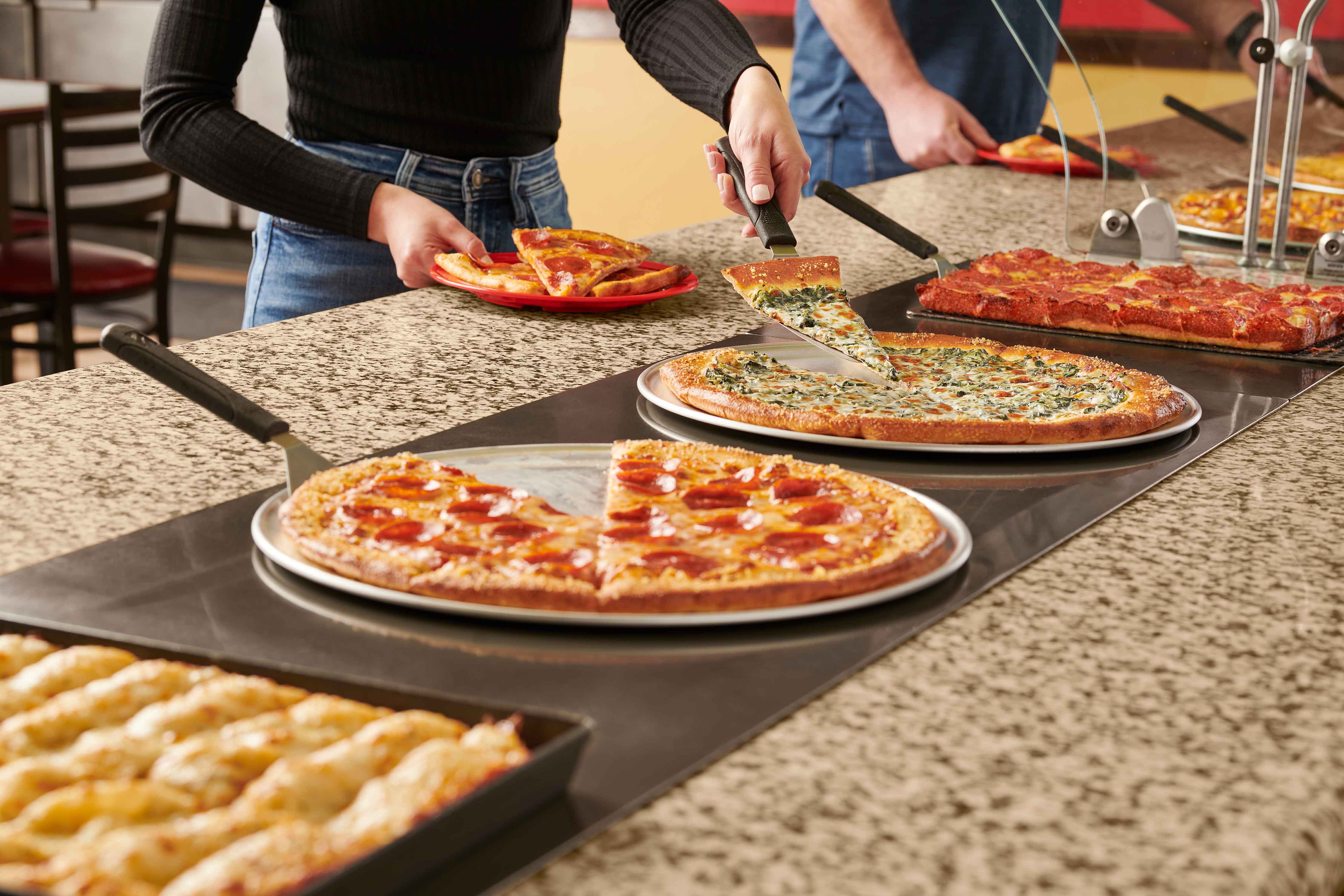 Pizza getting cut from a table of pizza buffet