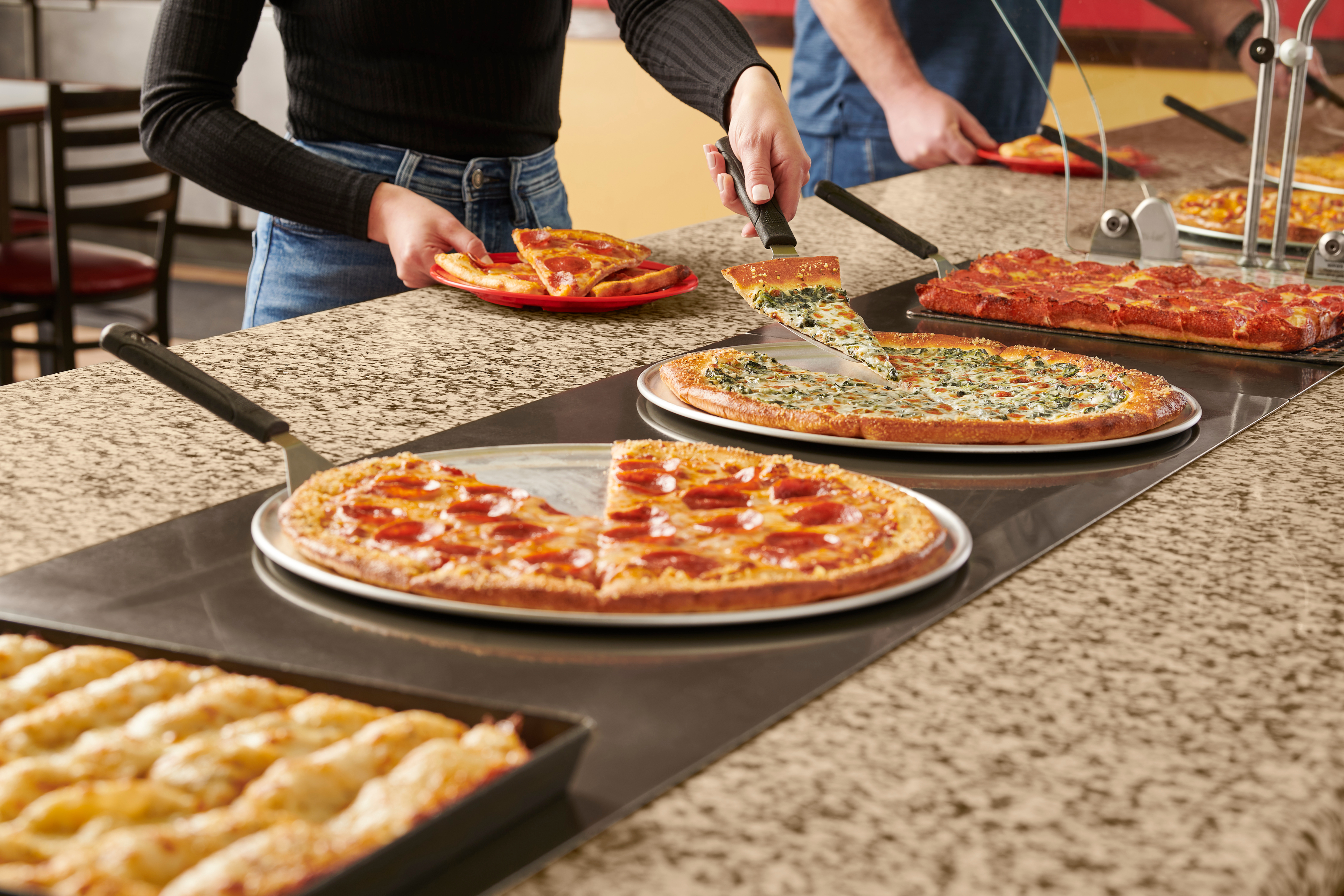 Two women sit at a table, each has a plate of pizza slices and a plate of salad. They are smiling as they each eat their own slice of pizza.